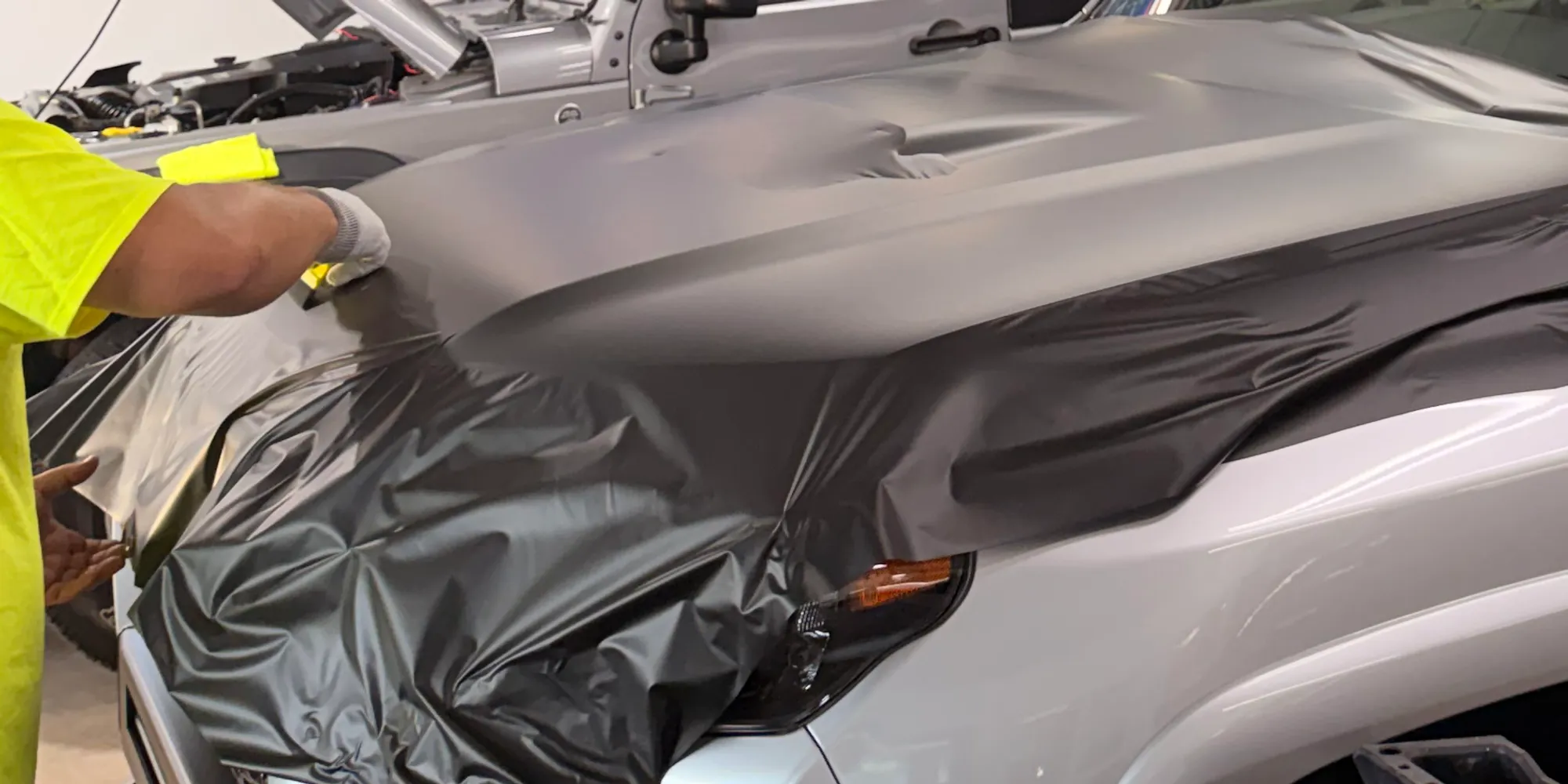 An installer's hands stretching black wrap film over a vehicle's hood in the install bay at 3920 12th St NW, Canton, OH 44708.